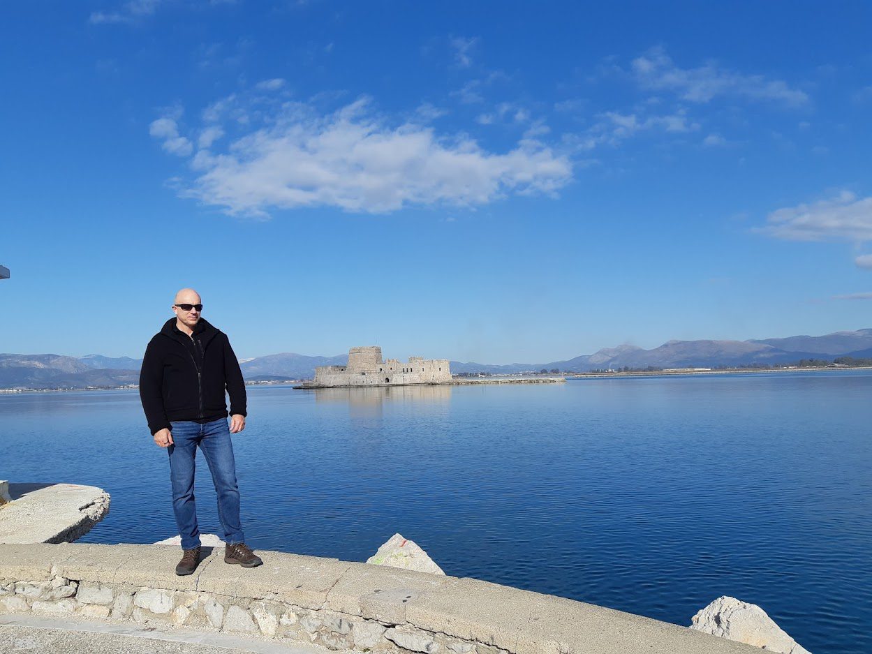 Dave Briggs visiting Nafplio in Greece, with the famous Bourtzi castle pictured behind