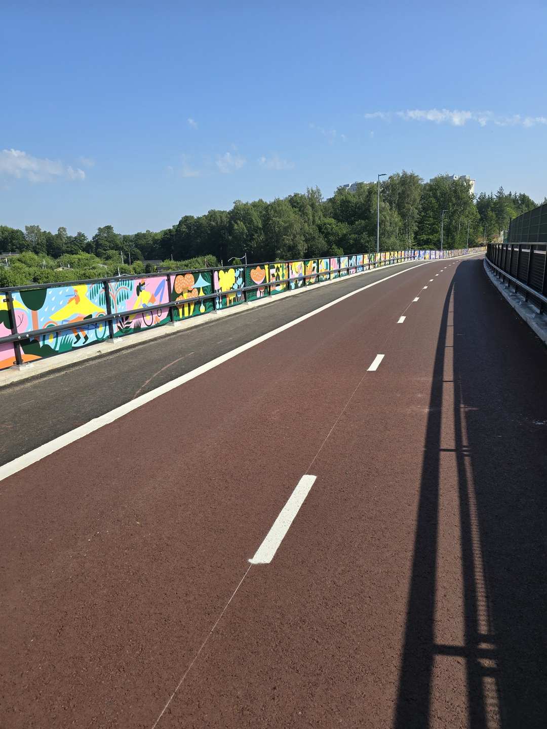 A wide dedicated cycleway with colourful murals painted on the bridge walls running through Finnish countryside