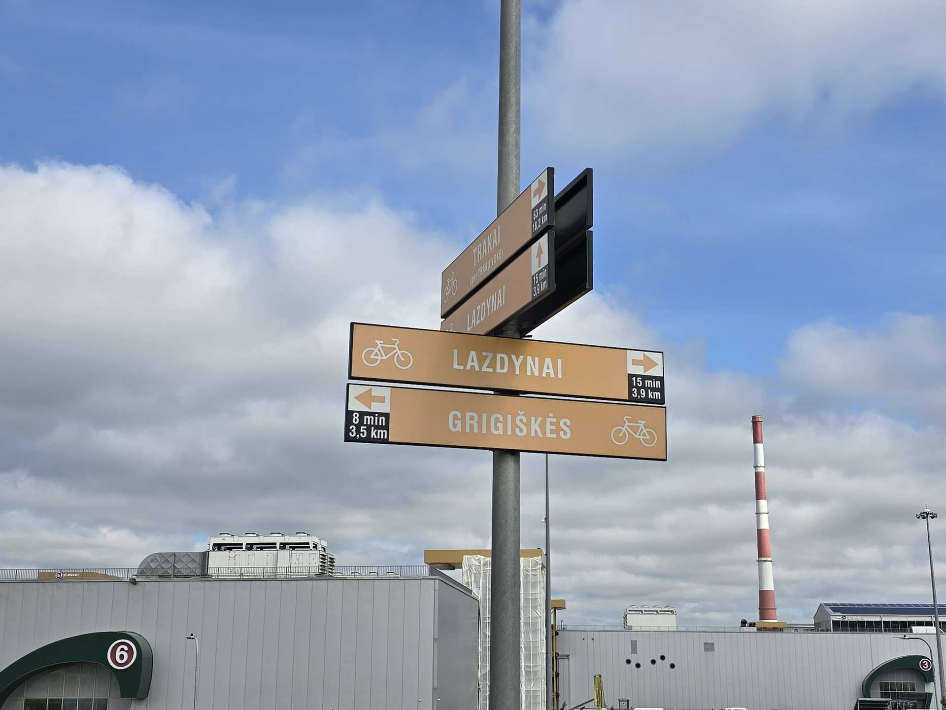 Brown directional cycle path signs showing distances to Lazdynai and Grigiškės in Lithuania